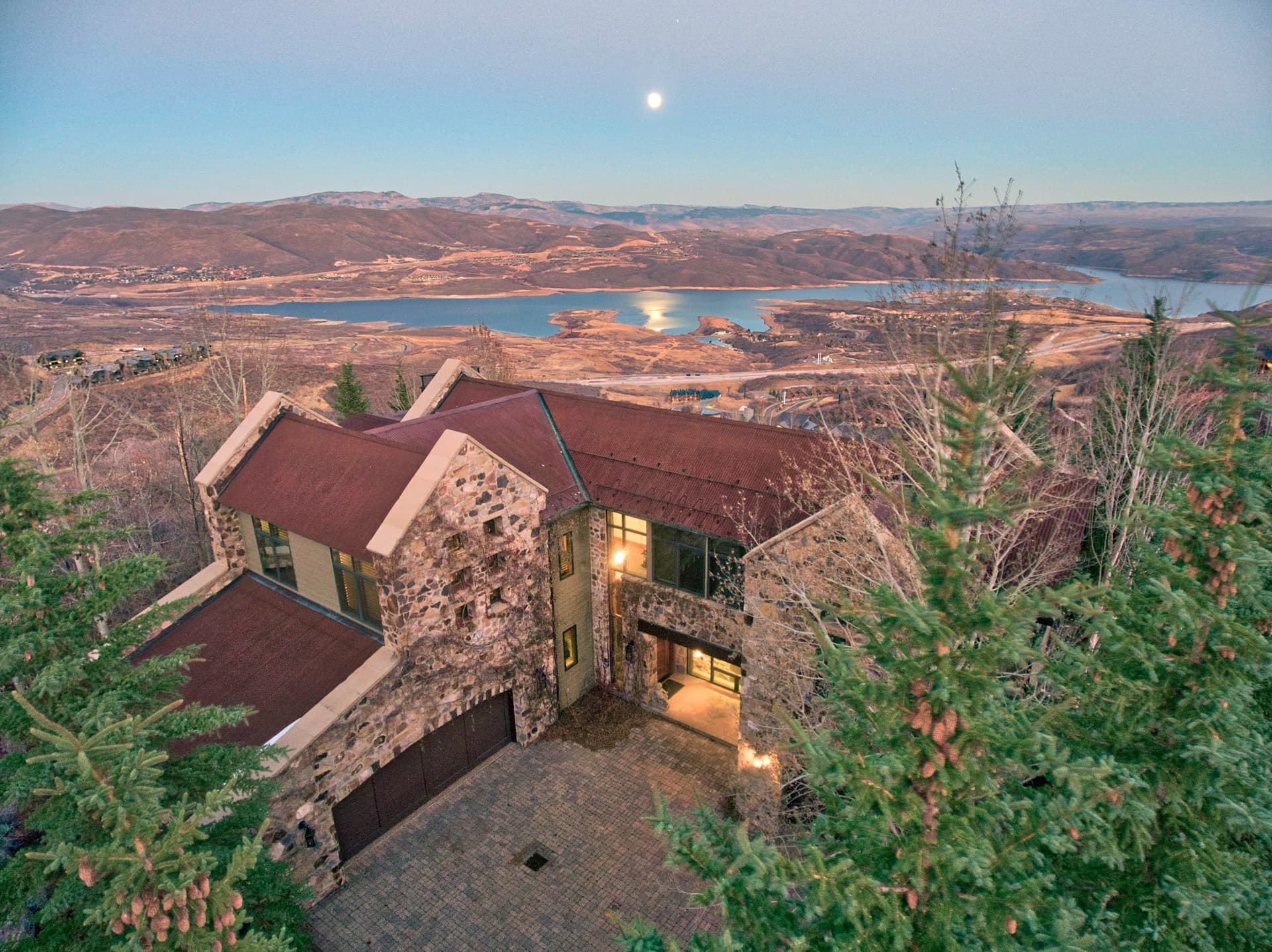 Exterior of mountain home at dusk with lake and moonlit sky in the background.