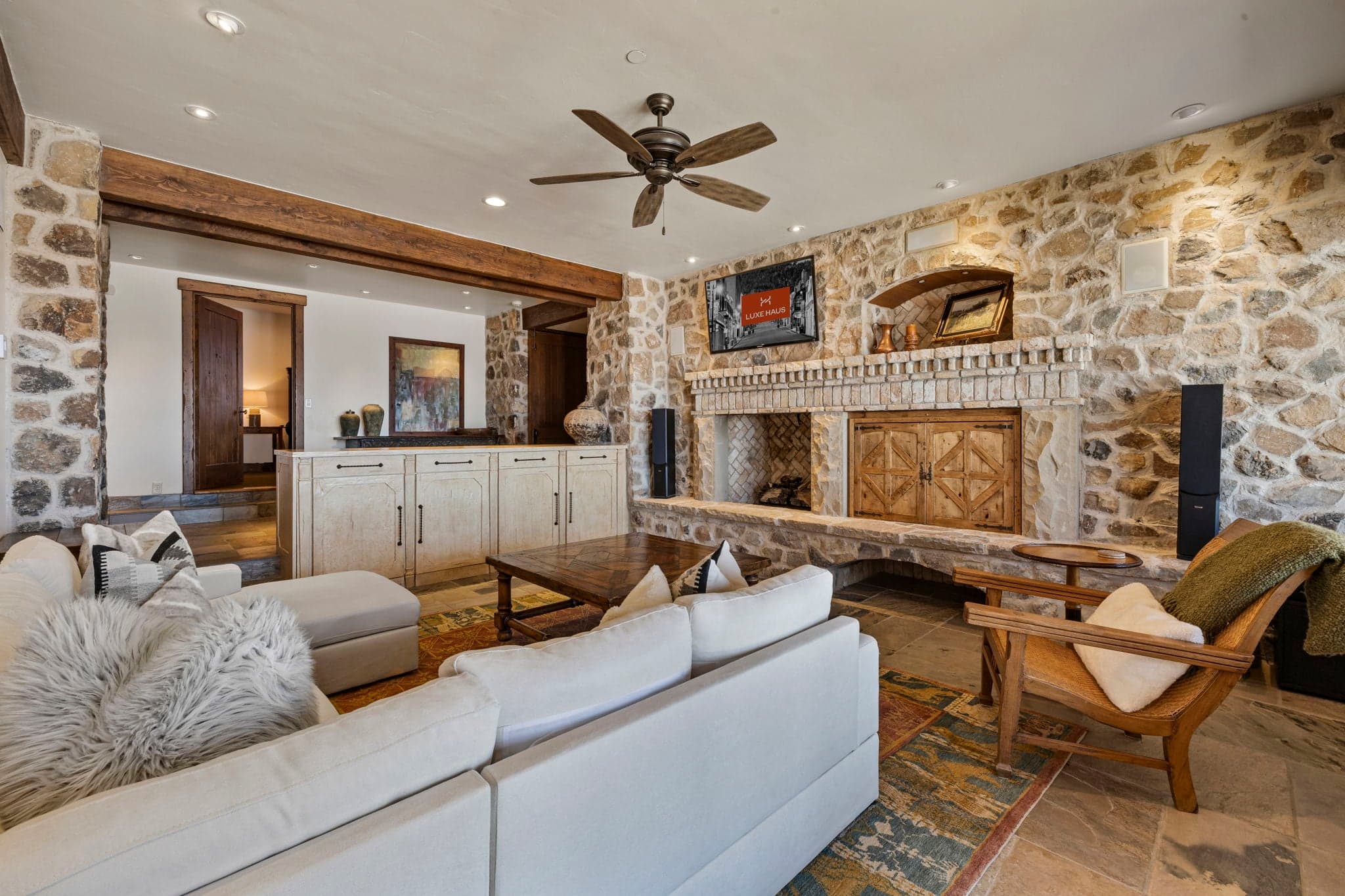 Lower-level living area with white sofas, stone walls, and rustic artwork.