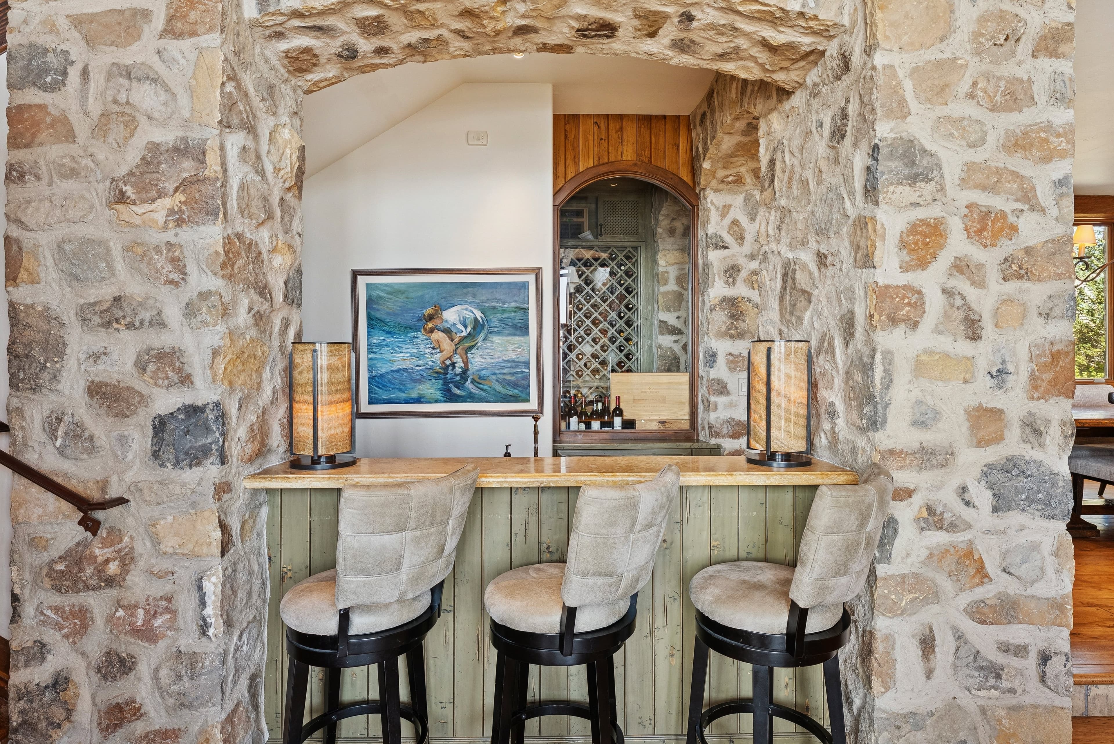 Stone bar with upholstered stools and built-in wine storage.