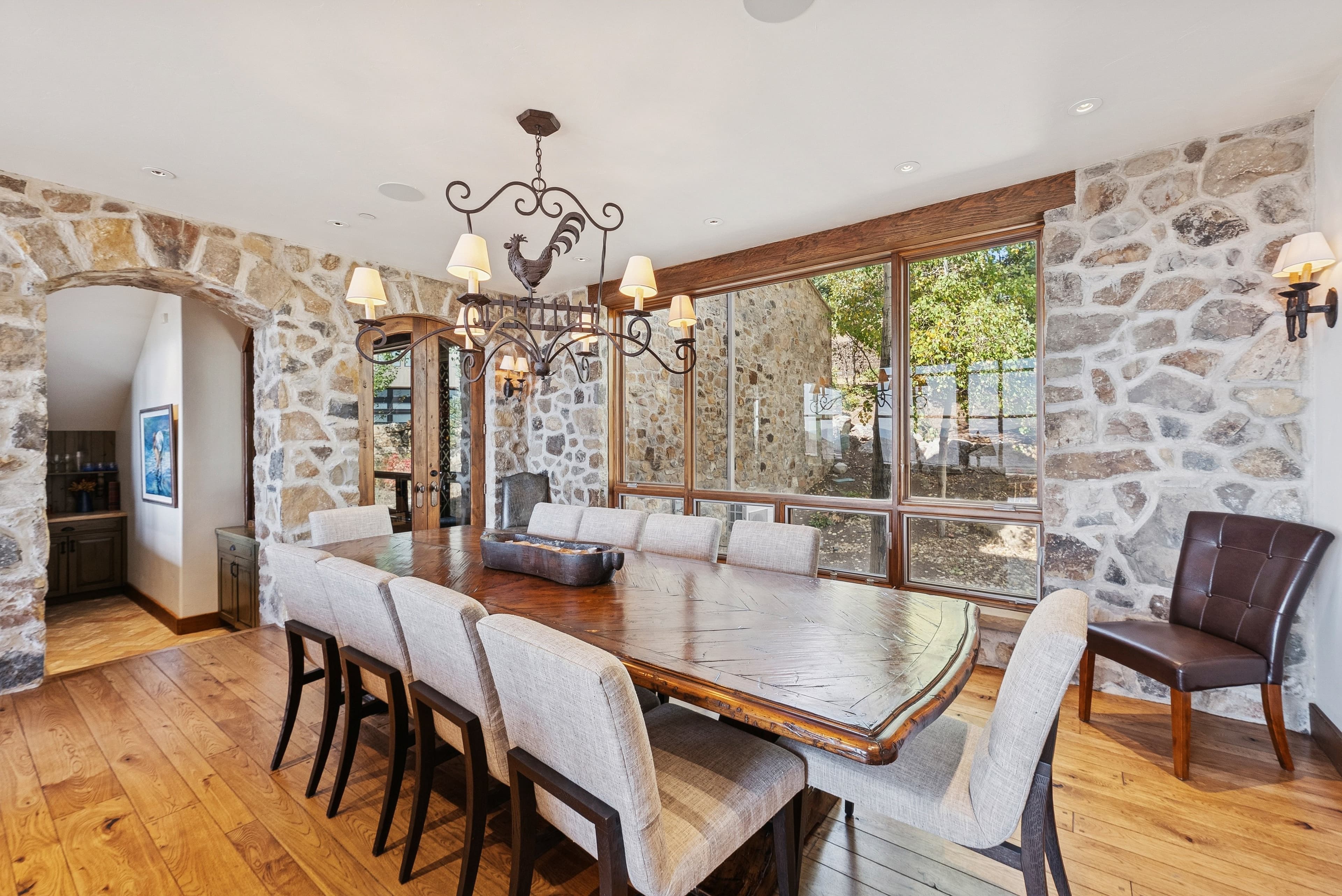 Formal dining room with long wooden table, upholstered chairs, chandelier, and stone walls.