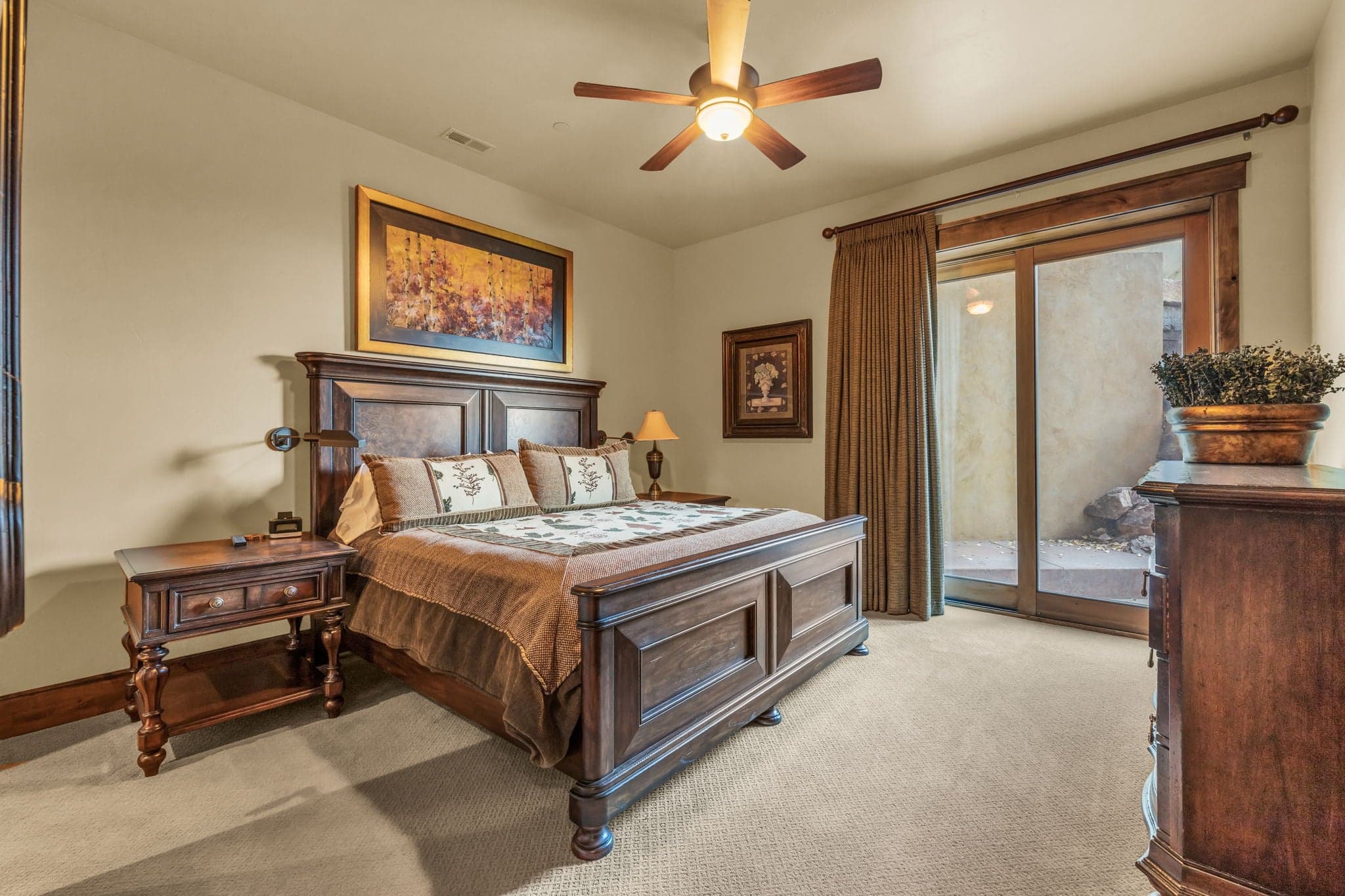 Bedroom with queen bed, paintings, and wooden shelves.