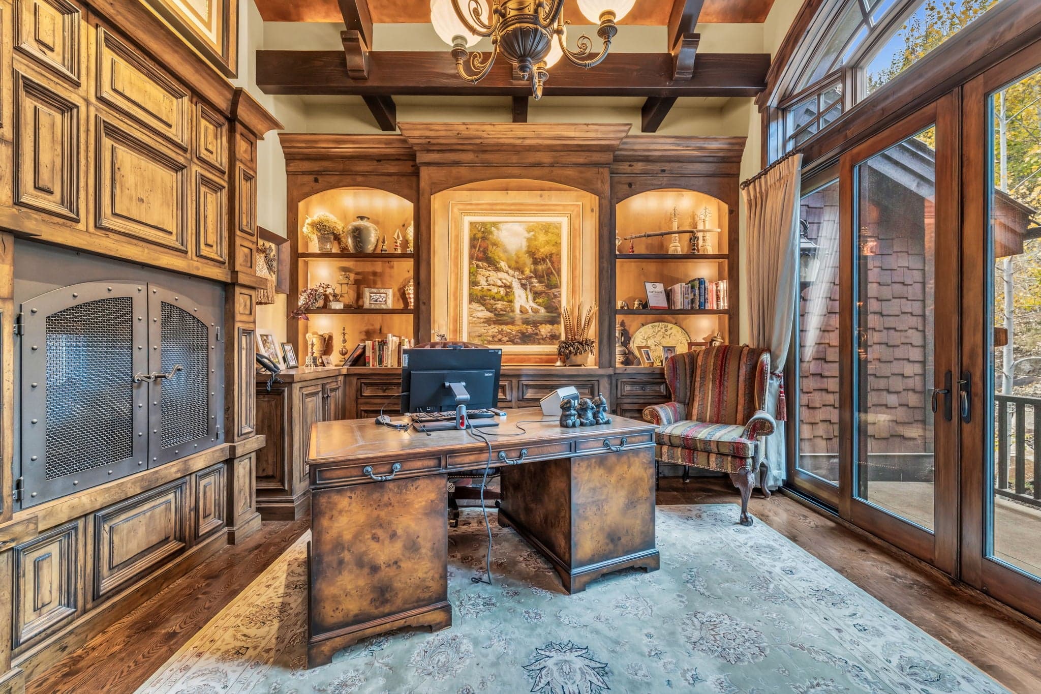 Home office with wooden desk, paintings, fireplace, and wooden shelves.