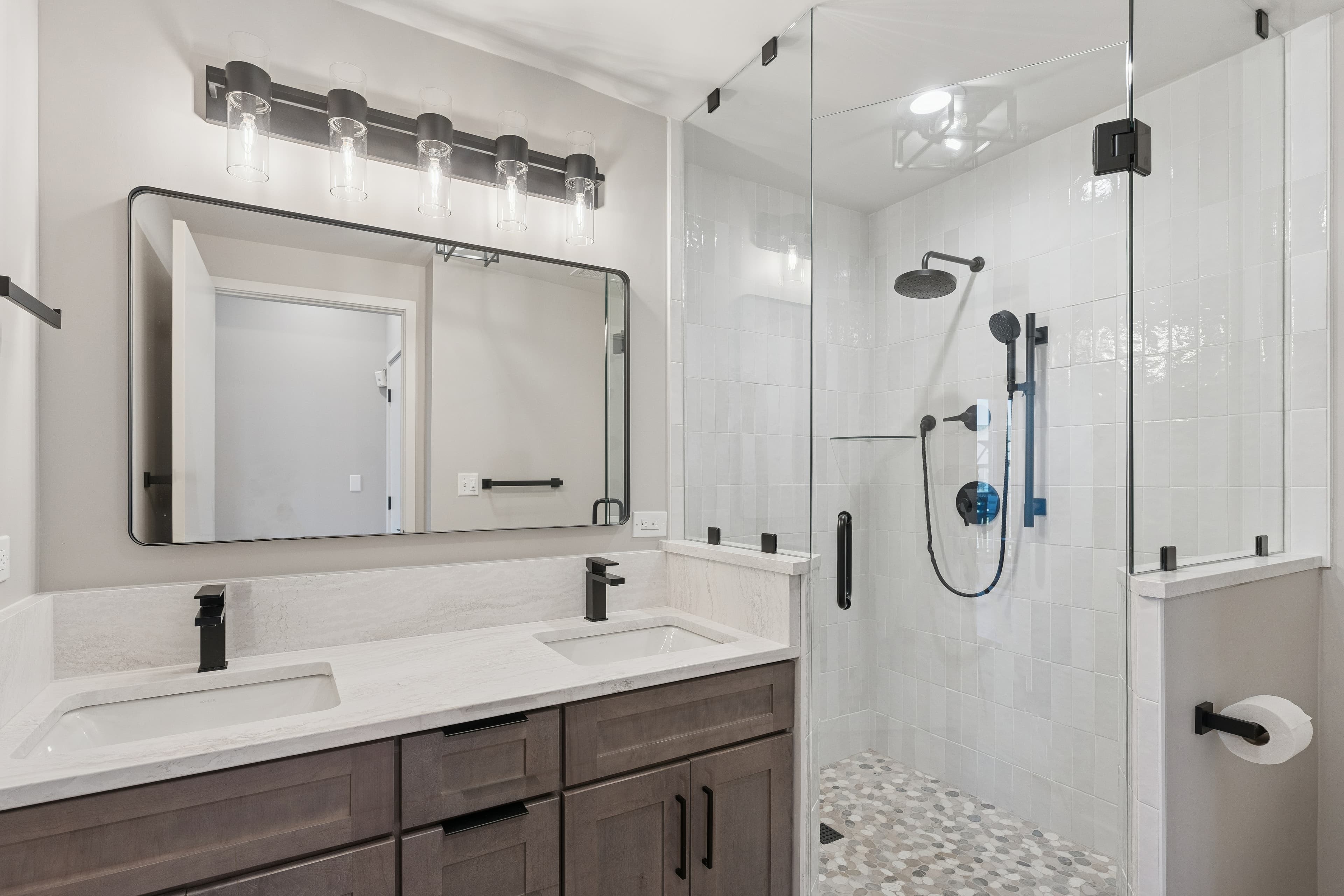 Spacious condo bathroom with double vanity, marble counters, and a walk-in glass shower.