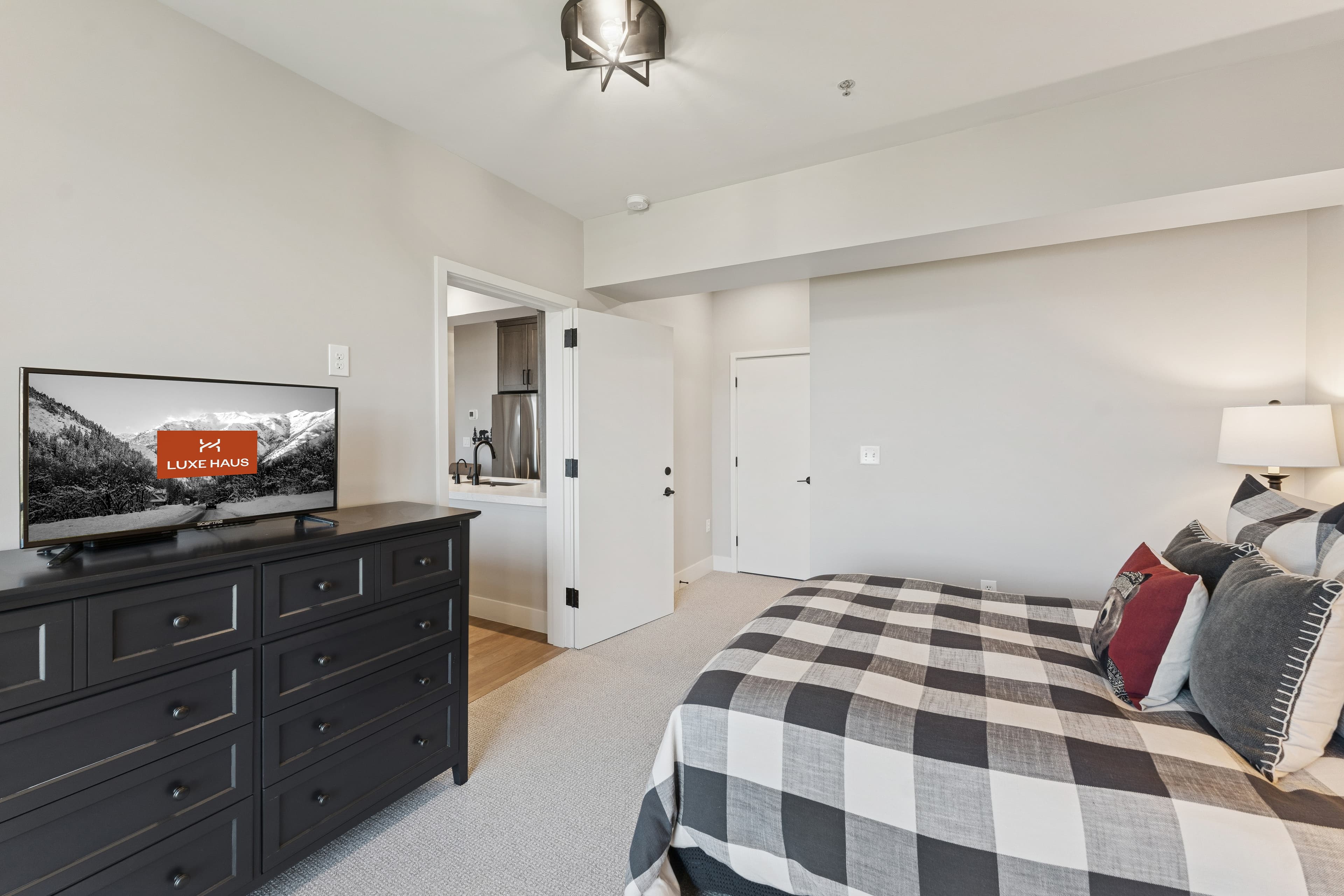 Spacious bedroom with checkered bedding, flat-screen TV, and dresser in a modern Park City condo.